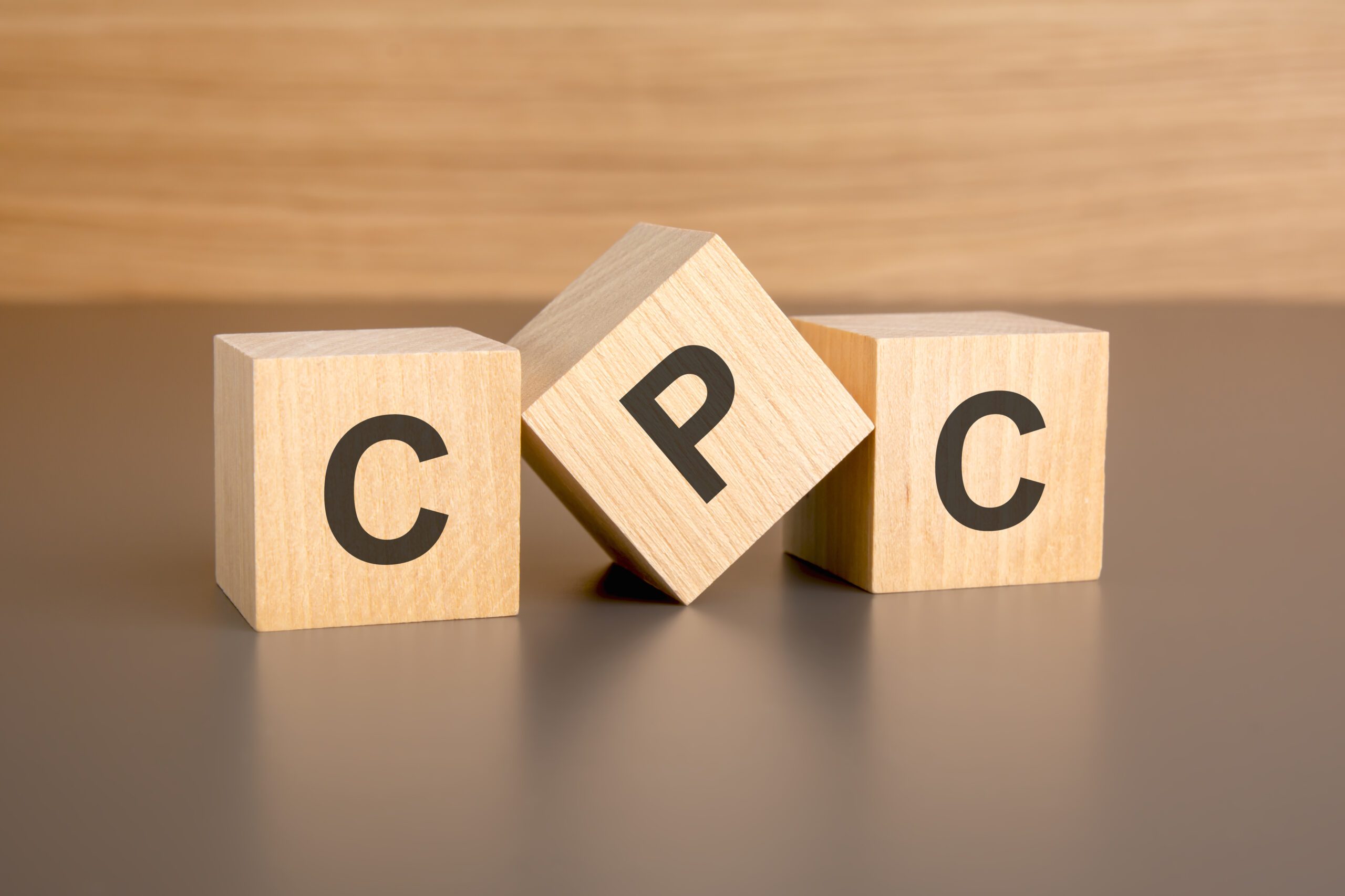 three wooden blocks on a brown background, with the abbreviation CPC – Cost Per Click